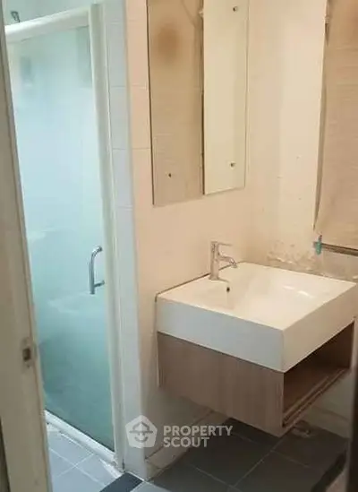 Modern bathroom with sleek sink and glass shower enclosure in contemporary apartment.