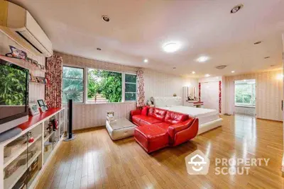 Spacious bedroom with vibrant red sofa and large windows offering lush garden views.