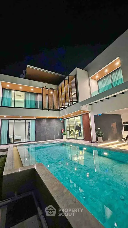 Luxurious modern villa with illuminated pool and expansive glass windows at night.