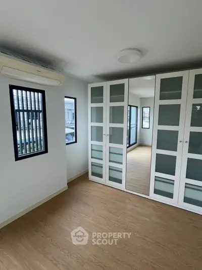 Spacious bedroom with mirrored wardrobe and large windows for natural light.