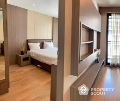 Modern bedroom with wooden flooring and built-in shelving, featuring a cozy bed and natural light.