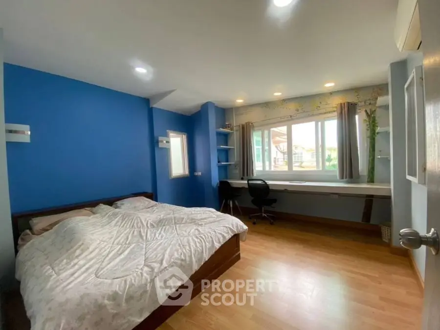 Spacious bedroom with blue walls, large window, and wooden flooring.