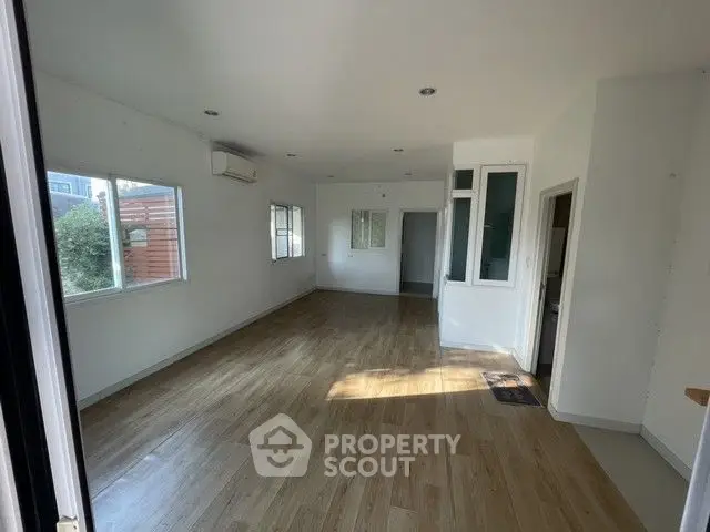 Spacious empty room with wooden flooring and large windows, ideal for customization.