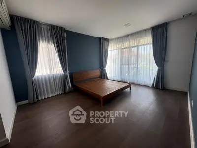 Spacious bedroom with wooden flooring and large windows for natural light.
