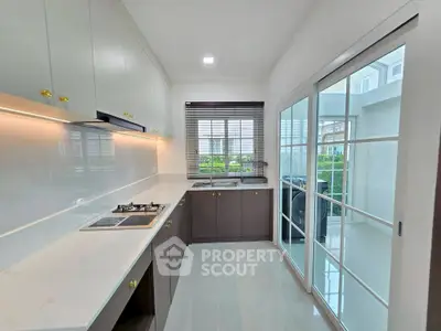 Modern kitchen with sleek cabinets and gas stove, bright natural light from large windows.
