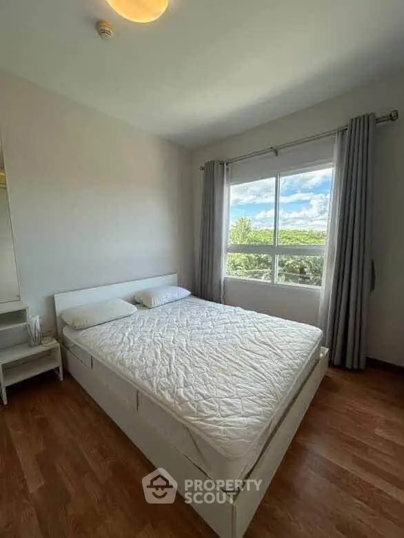 Bright bedroom with large window and scenic view, featuring a comfortable bed and wooden flooring.