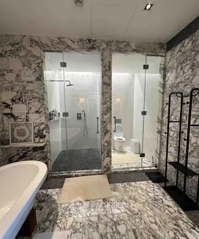 Luxurious marble bathroom with bathtub and glass-enclosed shower and toilet area.