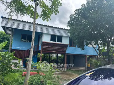 Charming elevated blue house with lush greenery and spacious outdoor area.