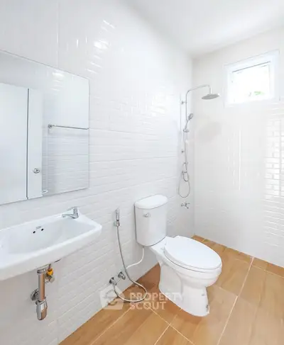 Modern bathroom with white tiles and natural light, featuring a shower and toilet.
