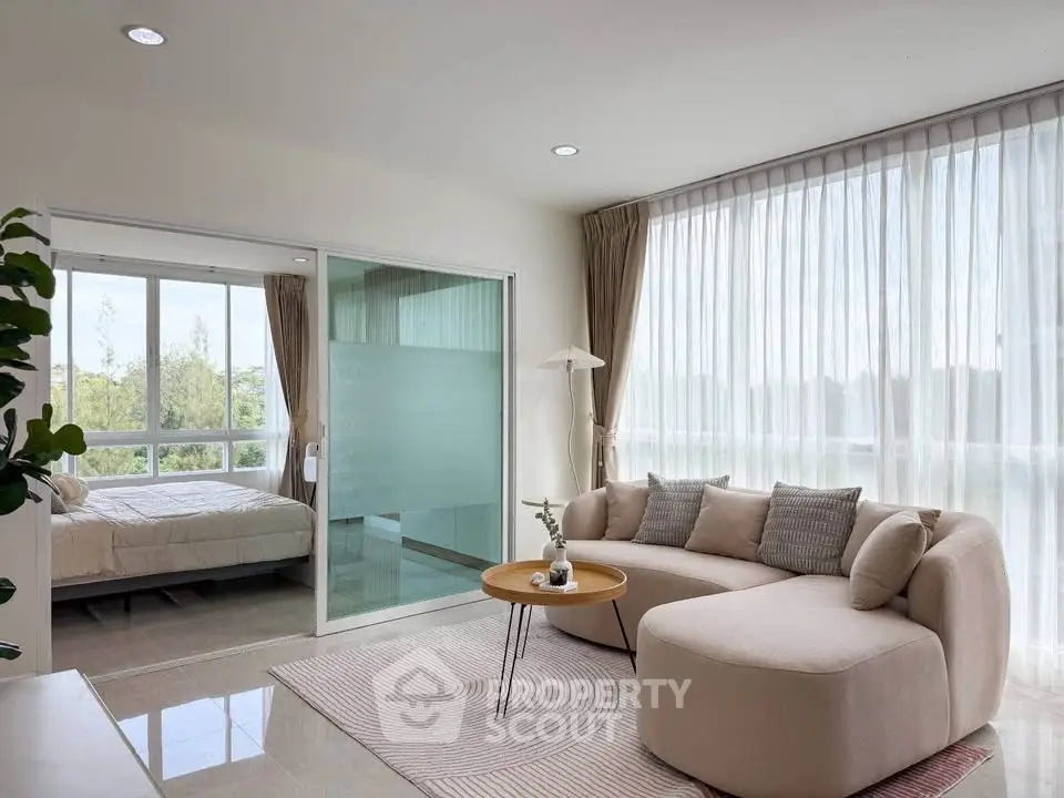 Modern living room with cozy sofa and large windows, adjacent to a bright bedroom with scenic views.