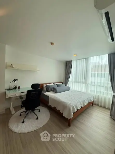 Modern bedroom with large windows, stylish desk, and cozy bed in a bright apartment.