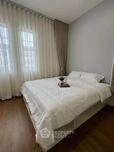 Cozy bedroom with elegant curtains and wooden flooring, perfect for relaxation.