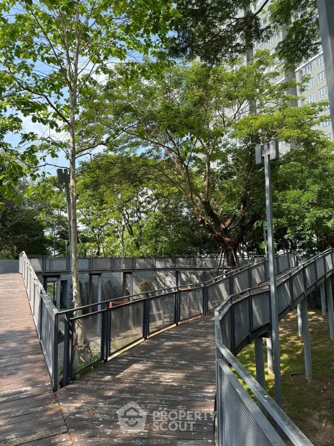 Modern urban park with lush greenery and sleek pathways near high-rise building.