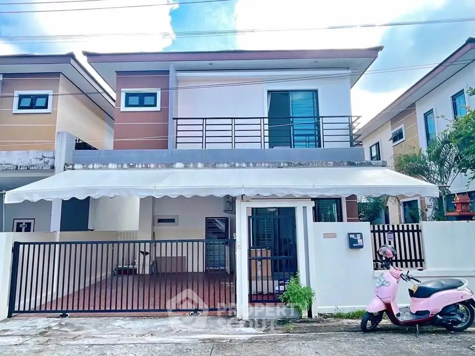 Modern two-story house with gated driveway and balcony in suburban neighborhood.