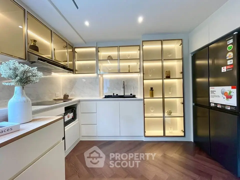 Modern kitchen with sleek cabinetry and gas stove, featuring elegant lighting and herringbone flooring.