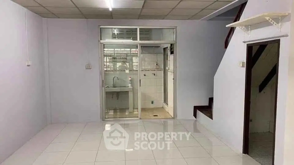 Spacious interior with tiled flooring and staircase, featuring a glass partition leading to a kitchen area.