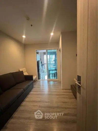 Modern living room with sleek flooring and cozy seating, leading to a bright balcony area.