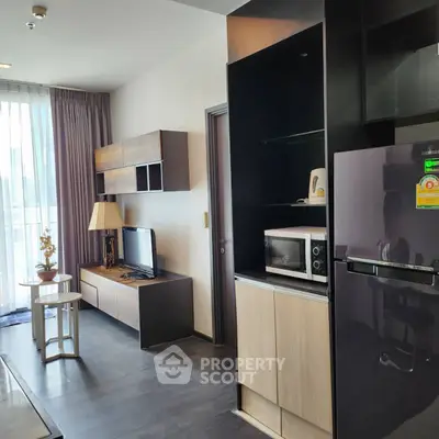 Modern living room with sleek furniture and large window, featuring a stylish entertainment center and kitchen appliances.