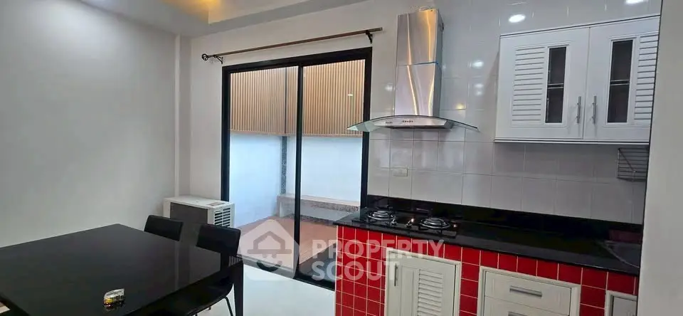 Modern kitchen with sleek black dining table and gas stove, adjacent to a balcony.