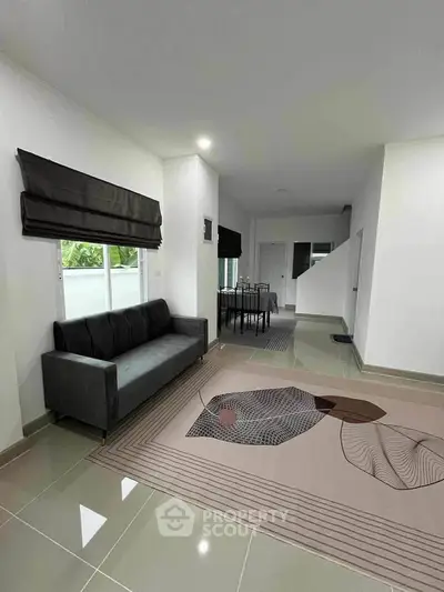 Modern living room with sleek sofa and artistic rug, leading to dining area in open layout.