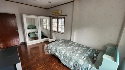 Spacious bedroom with wooden flooring and large mirror reflecting natural light