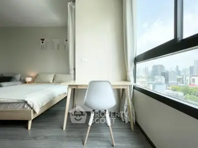 Modern bedroom with study area and city view, featuring sleek furniture and large windows.