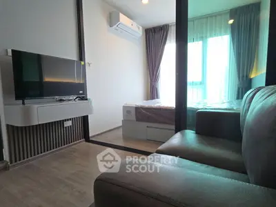 Modern apartment interior with cozy living room and bedroom separated by glass partition, featuring sleek furniture.