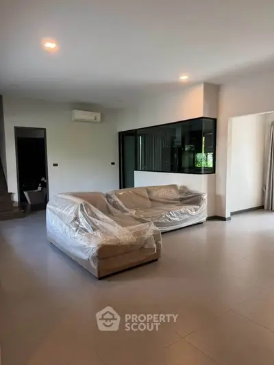 Spacious modern living room with covered sofas and large windows in a contemporary home.