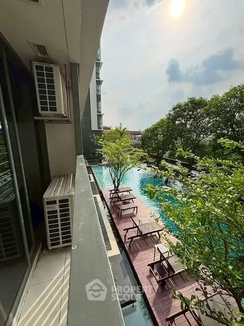 Luxurious apartment balcony overlooking a stunning pool and lush greenery, perfect for relaxation and leisure.