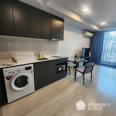 Modern studio apartment with sleek kitchen and dining area, featuring washing machine and stylish decor.