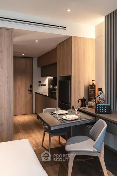 Modern studio apartment with sleek kitchen and dining area, featuring wood accents and contemporary design.