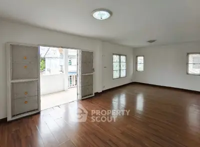 Spacious empty room with wooden flooring and balcony access in modern home.