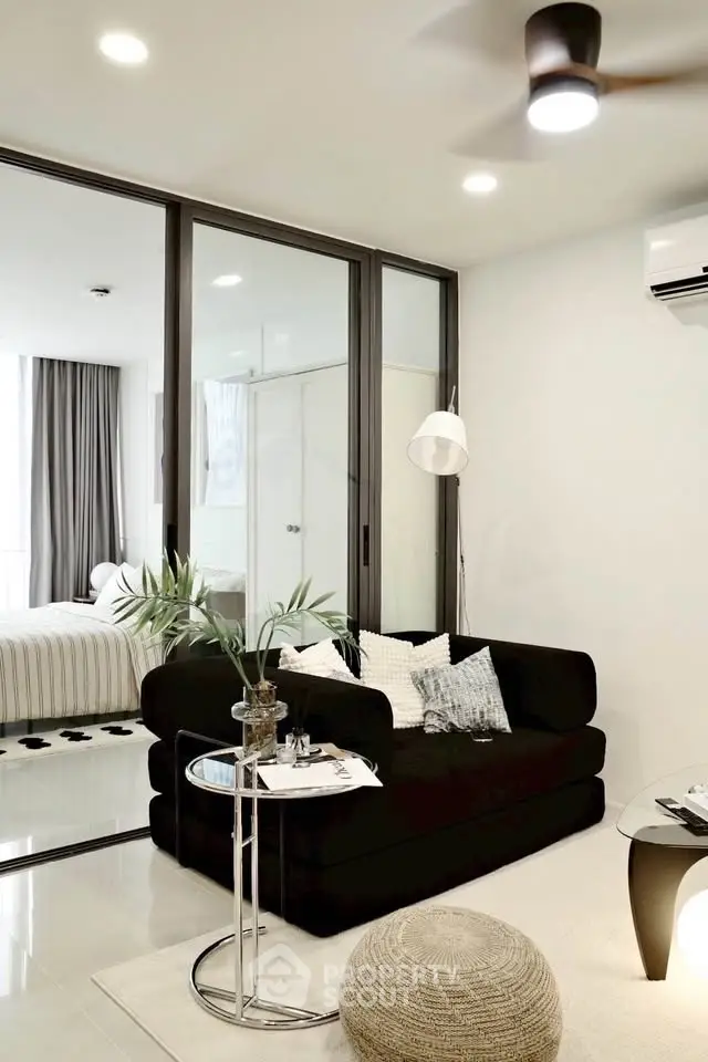 Modern living room with sleek black sofa and glass partition to bedroom