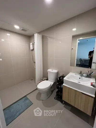 Modern bathroom with sleek fixtures and neutral tiles, featuring a shower and vanity unit.