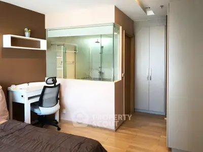 Modern bedroom with study area and glass-walled bathroom, featuring sleek design and ample natural light.