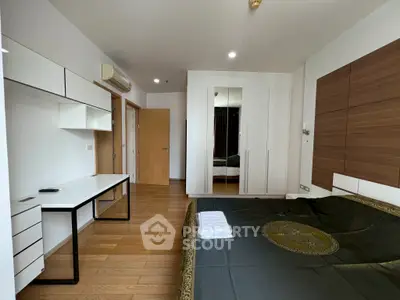 Modern bedroom with sleek furniture and wooden flooring, featuring a stylish desk and built-in wardrobe.
