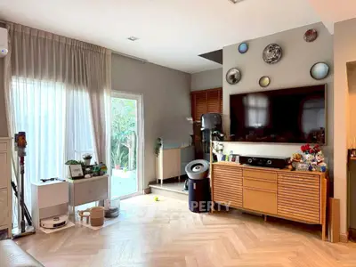 Stylish living room with modern decor and large TV, featuring elegant wooden flooring and garden view.