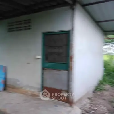 Exterior view of a small, rustic building with metal door and corrugated roof.