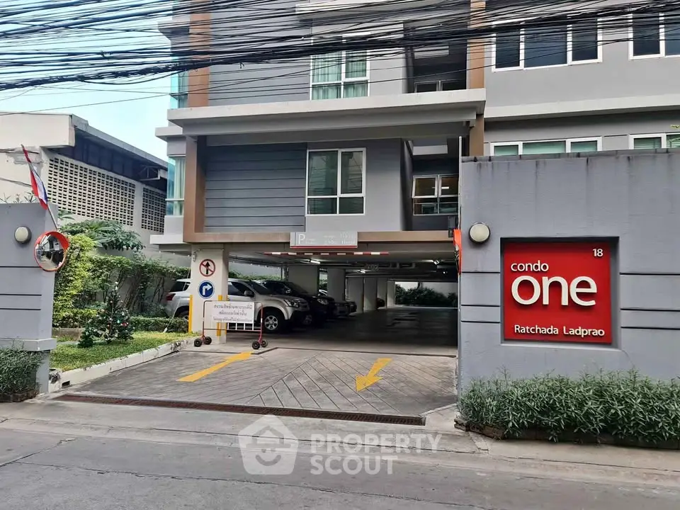 Modern condo entrance with parking area and clear signage in urban setting.