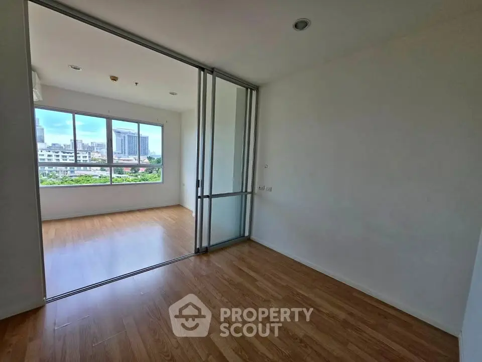 Spacious apartment with sliding glass doors and city view, featuring elegant wooden flooring.