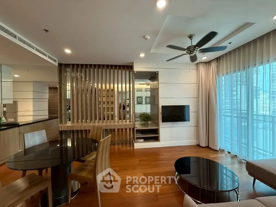 Modern living room with wooden flooring, ceiling fan, and large windows offering city views.