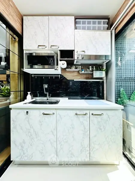 Modern compact kitchen with marble cabinets and sleek appliances in a bright, stylish apartment.