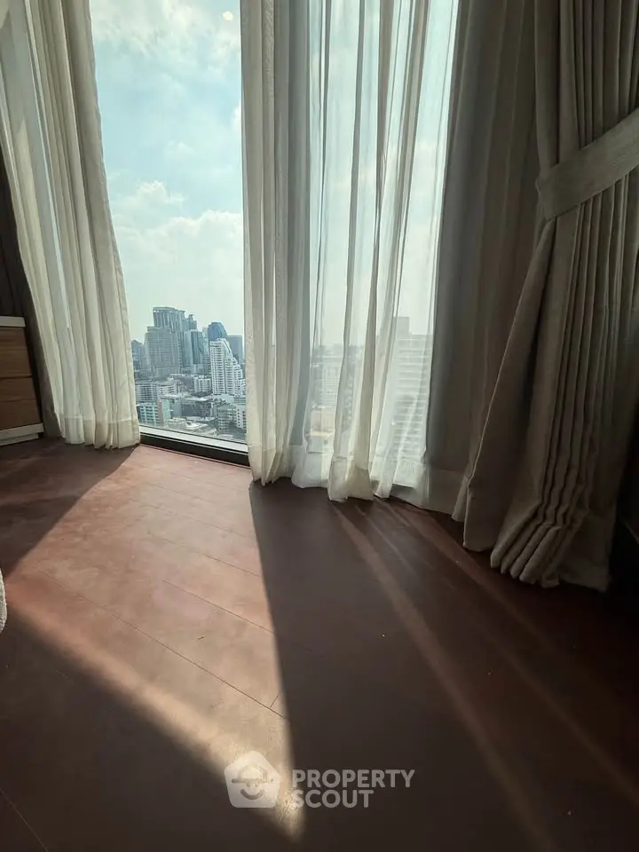 Stunning city view from a high-rise apartment with floor-to-ceiling windows and elegant curtains.
