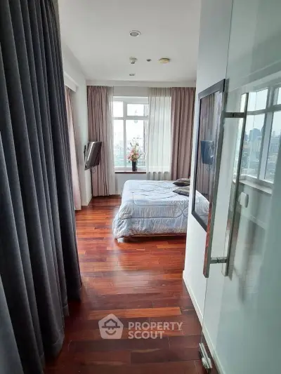 Luxurious bedroom with hardwood floors and city view, featuring elegant curtains and modern decor.