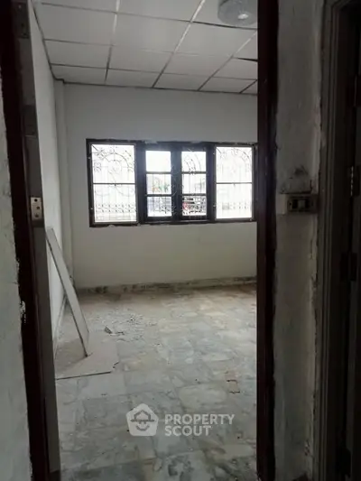 Spacious room with tiled floor and large window, ideal for renovation.