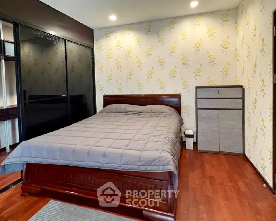 Cozy bedroom with elegant wooden flooring and stylish floral wallpaper, featuring a comfortable bed and sleek wardrobe.
