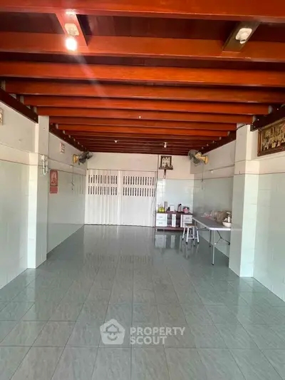 Spacious tiled room with wooden ceiling beams and minimal furnishings, ideal for versatile use.
