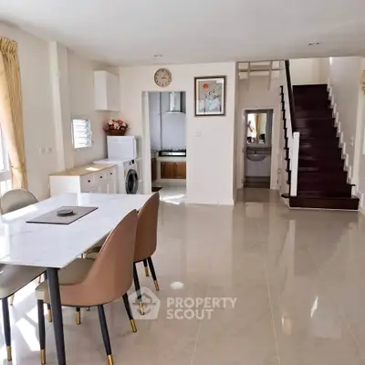 Spacious modern living area with dining table, washing machine, and staircase in a bright open layout.