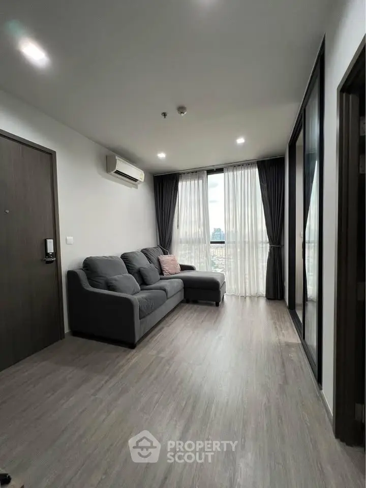 Modern living room with sleek gray sofa and large windows offering natural light and city views.