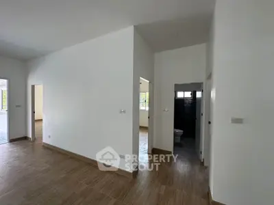 Spacious modern interior with wooden flooring and white walls, featuring multiple doorways and natural light.